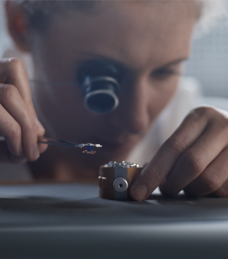 Eine Uhrmacherin setzt unter dem Mikroskop ein Bauteil in ein Rolex Uhrwerk ein